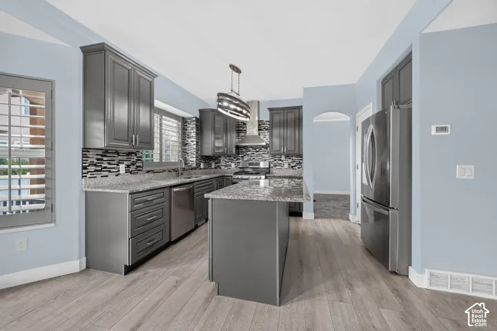 Kitchen featuring gray cabinetry, stone-finish countertops, stainless steel appliances, a mosaic tile backsplash, and wood-finish flooring