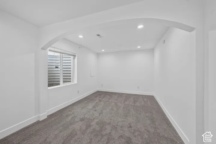 Recessed lighting, arched doorway, egress window with blinds, and neutral carpeting