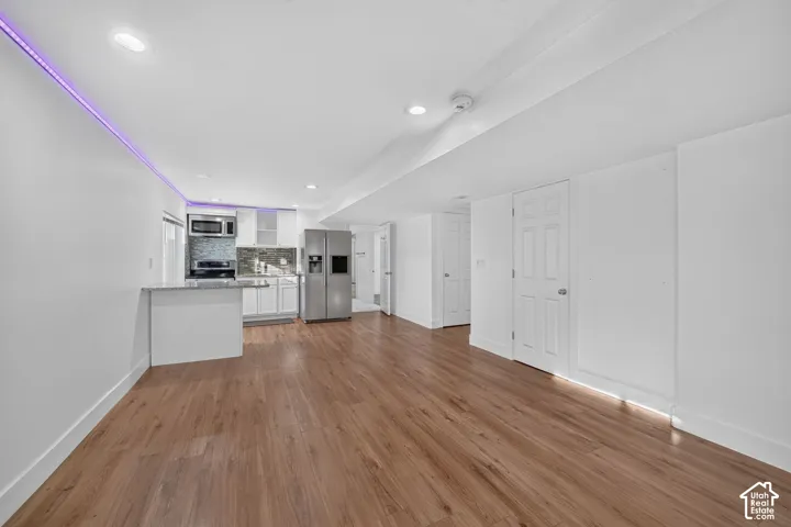 Wood-finish flooring throughout, recessed lighting, and a modern kitchen featuring stainless steel appliances, white cabinetry, and a tile backsplash