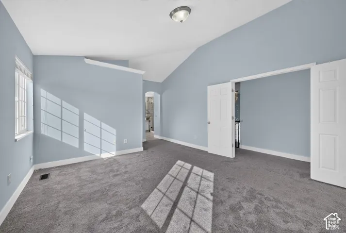 Vaulted ceiling, gray carpet, multiple white doors, window with white grid, archway