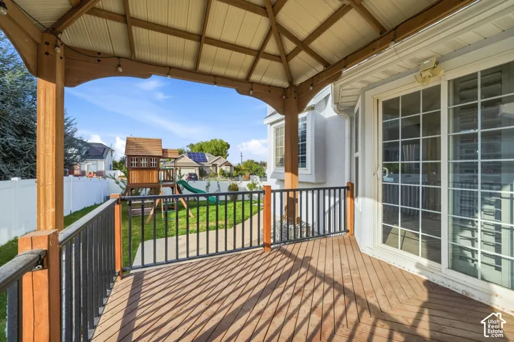 Covered outdoor deck with wood-finish flooring, metal railing, and white vinyl fence