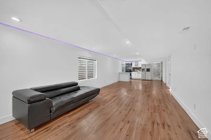 Spacious open-concept living area showcasing wide-plank wood-finish flooring, recessed ceiling lighting with accent LED strip, and abundant natural light from shuttered windows