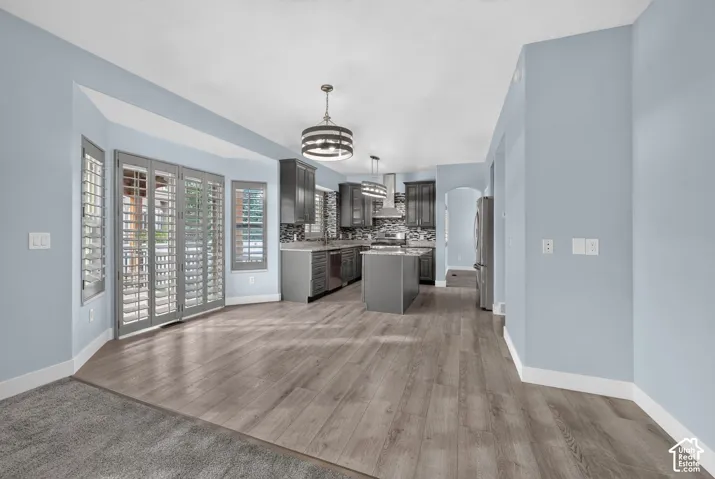 Open-concept living space with wood-finish flooring, a contemporary chandelier, and a kitchen featuring dark cabinetry, stainless steel appliances, and a central island