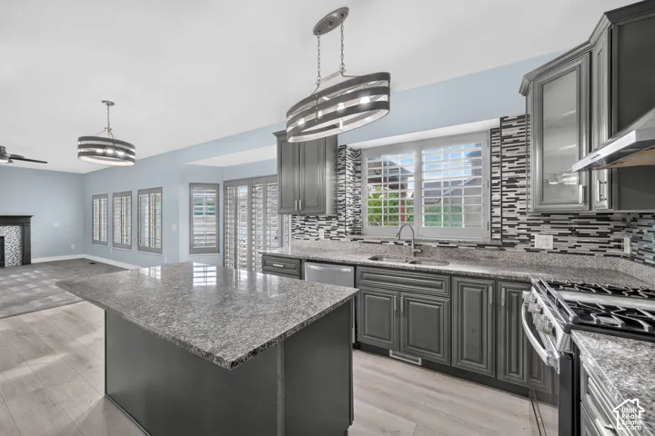 Kitchen featuring dark gray cabinetry, light granite countertops, stainless steel appliances, and a mosaic tile backsplash