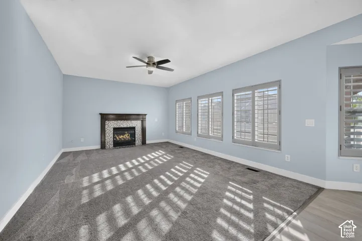 Spacious room featuring a fireplace with a mosaic tile surround and dark wood mantle, a ceiling fan, multiple windows with plantation shutters, and light blue walls