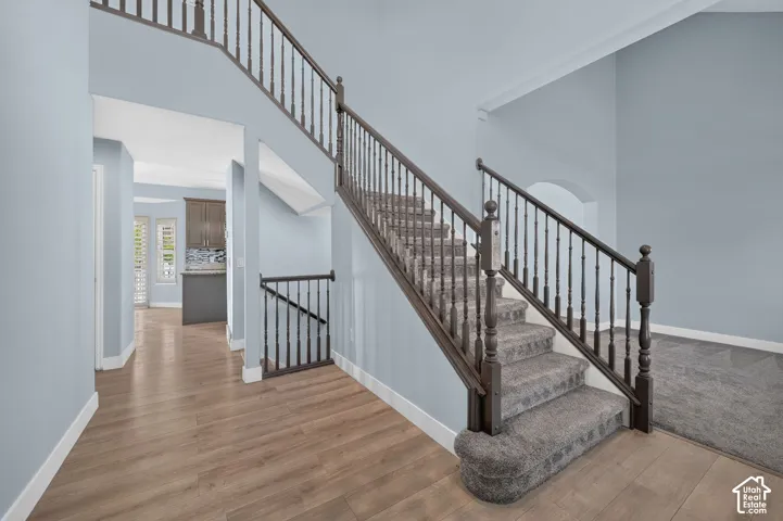 Double-height entry with wood-finish flooring, carpeted staircase, and dark wood balusters