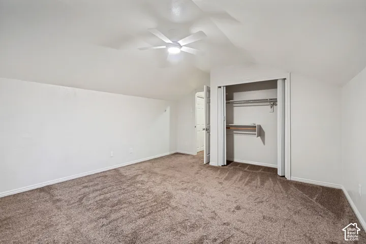Spacious room with sloped ceiling, brown carpet flooring, and a ceiling fan