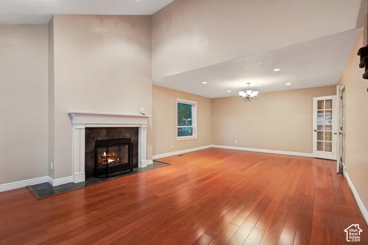 Hardwood flooring, fireplace with white mantel, recessed lighting, chandelier, and a French door