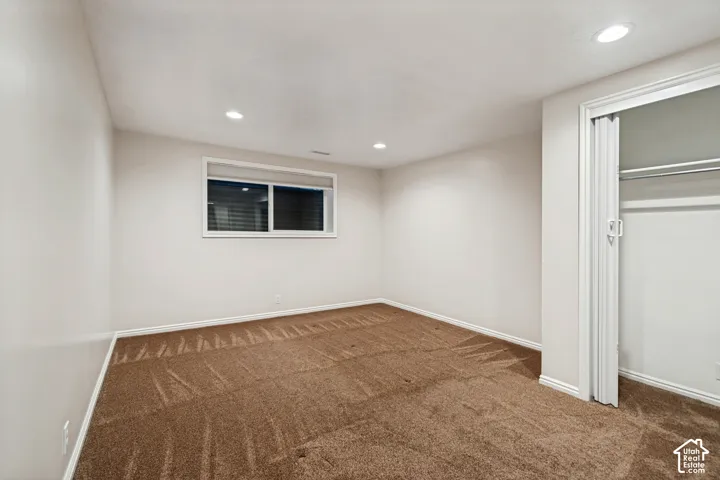 Room featuring brown carpeting, white walls, a recessed light fixture, a window with blinds, and a built-in closet with bifold doors