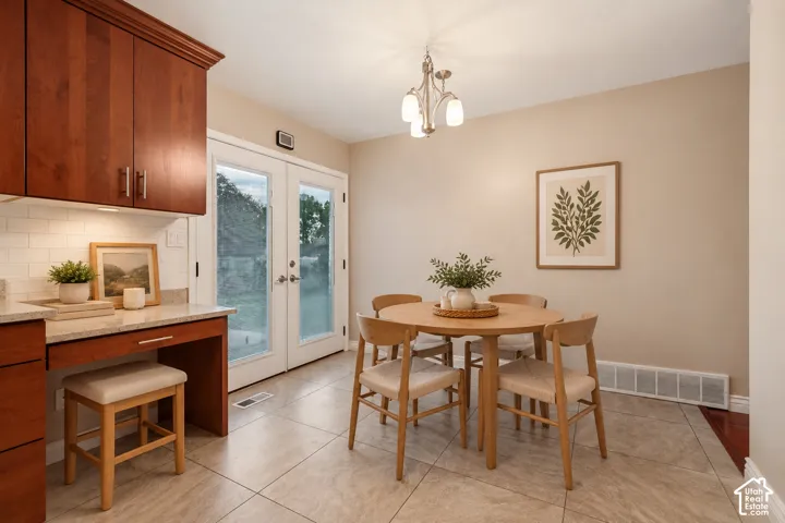 This is an AI furnished room Dining area featuring tile flooring, built-in cabinetry with stone countertops, double glass pane doors, and a multi-arm overhead light fixture