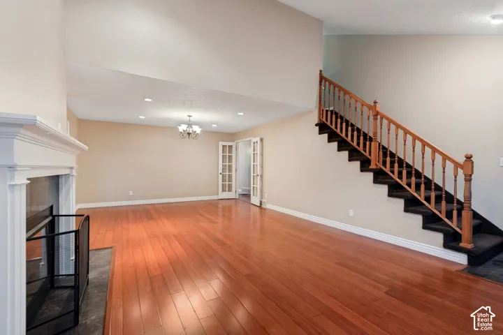 Hardwood flooring, vaulted ceiling, fireplace with white mantel, French doors, and a staircase with wood railing