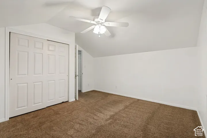 Sloped ceiling room featuring a white ceiling fan with light fixture, brown carpet flooring, and white bi-fold closet doors