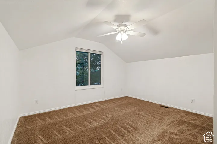 Vaulted ceiling with a ceiling fan light fixture, window, and brown carpeting