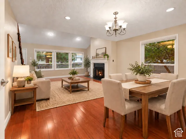 This is an AI furnished room. Open-concept living and dining area featuring wood-finish flooring, vaulted ceilings, recessed lighting, a multi-arm chandelier, and a fireplace with a mantel