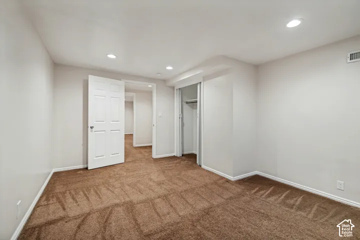 Recessed ceiling lighting, white six-panel door, brown carpet flooring, and a closet with sliding doors