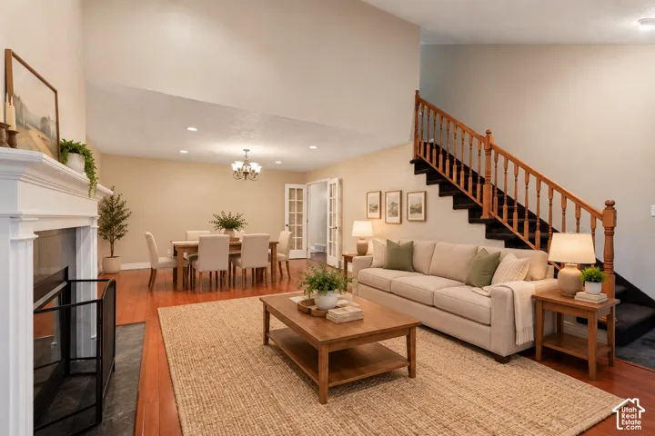 This is an AI furnished room Vaulted ceilings, wood-finish flooring, white mantel fireplace with stone hearth, wooden staircase with traditional banister, and glass-paneled double doors