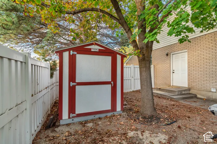 White vinyl privacy fence surrounding the property, a red and white shed, mature trees, and a brick exterior with white siding