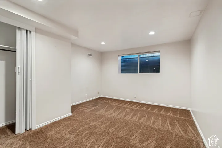 Recessed ceiling lighting, white walls, brown carpet, window with horizontal blinds, bi-fold closet doors