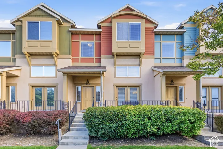 Multi-story townhome exterior featuring an inviting covered entry, a private balcony, and decorative landscaping