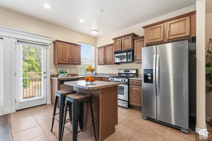 Kitchen featuring wood-finish cabinetry, stainless steel appliances, a center island with countertop seating, and tile flooring