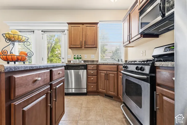 Kitchen featuring wood-finish cabinetry, stainless steel appliances, and a tile floor