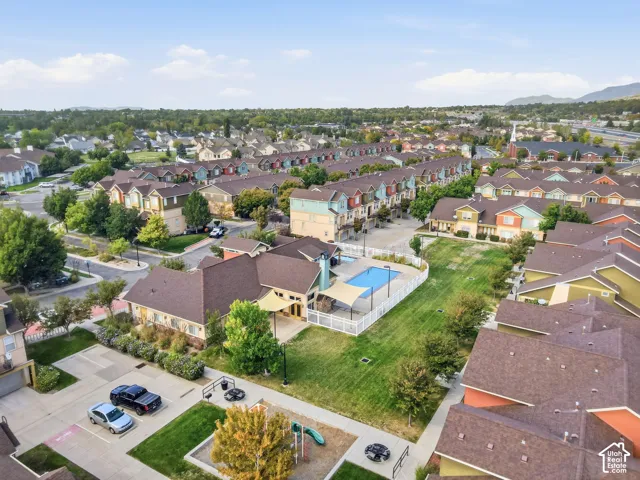 Aerial view showcasing an in-ground swimming pool, expansive manicured lawn, mature landscaping, and a multi-car driveway within an established residential community