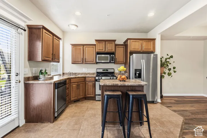 Kitchen featuring wood cabinetry, stainless steel appliances, a center island with seating, and tile flooring