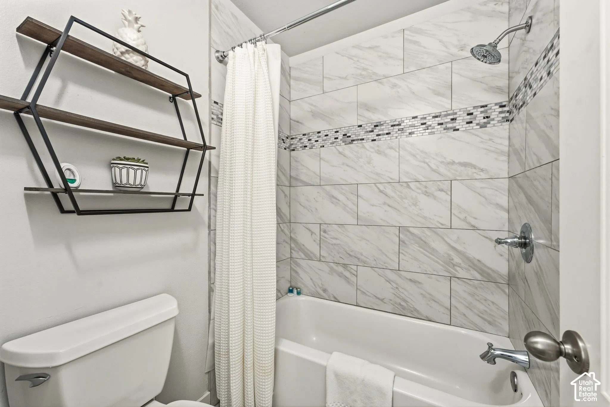 Bathtub with subway tile surround, mosaic accent strip, and a chrome showerhead