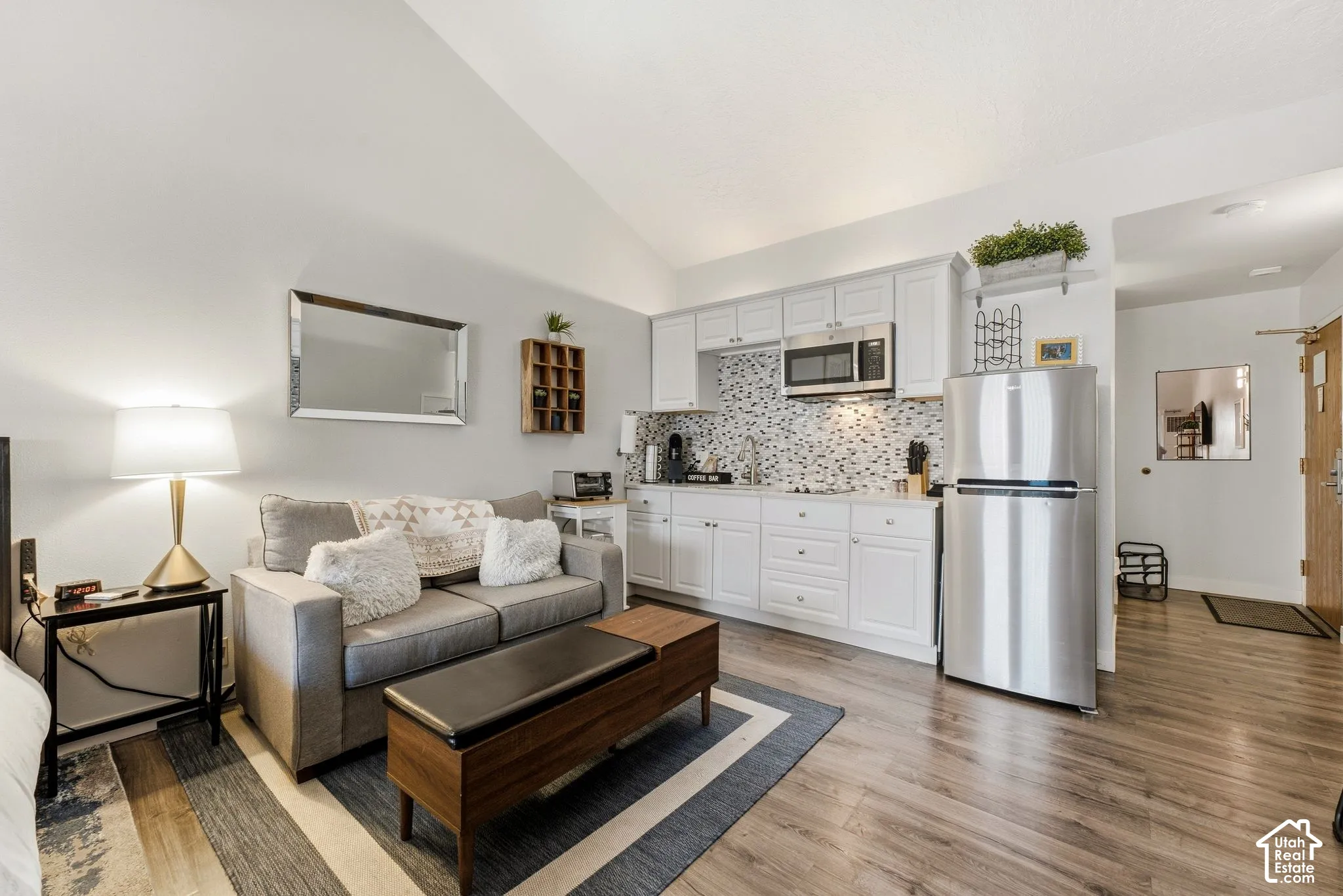 Vaulted ceiling above a compact living space featuring wood-finish flooring, white cabinetry, a mosaic tile backsplash, and stainless steel appliances