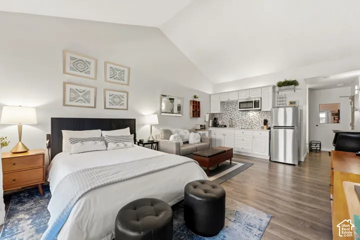 Vaulted ceiling, wood-finish flooring, white cabinetry, tile backsplash, and stainless steel appliances