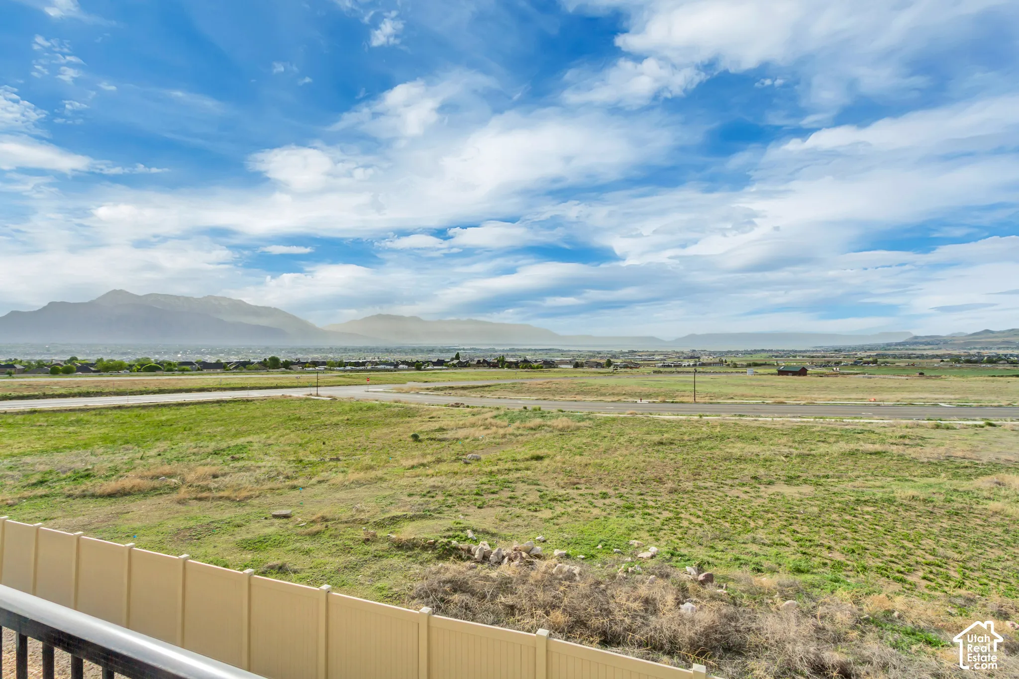 Expansive landscape featuring open fields, distant mountain ranges, and a clear sky with scattered clouds