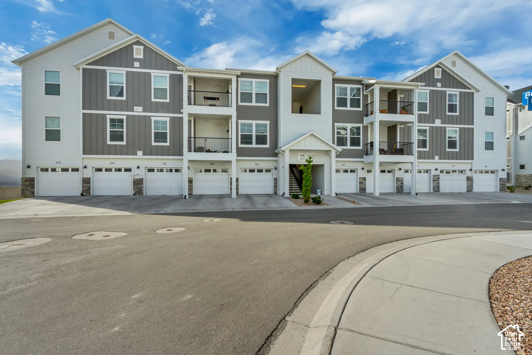 Multi-story residential building with attached garages, individual balconies, and stone veneer accents