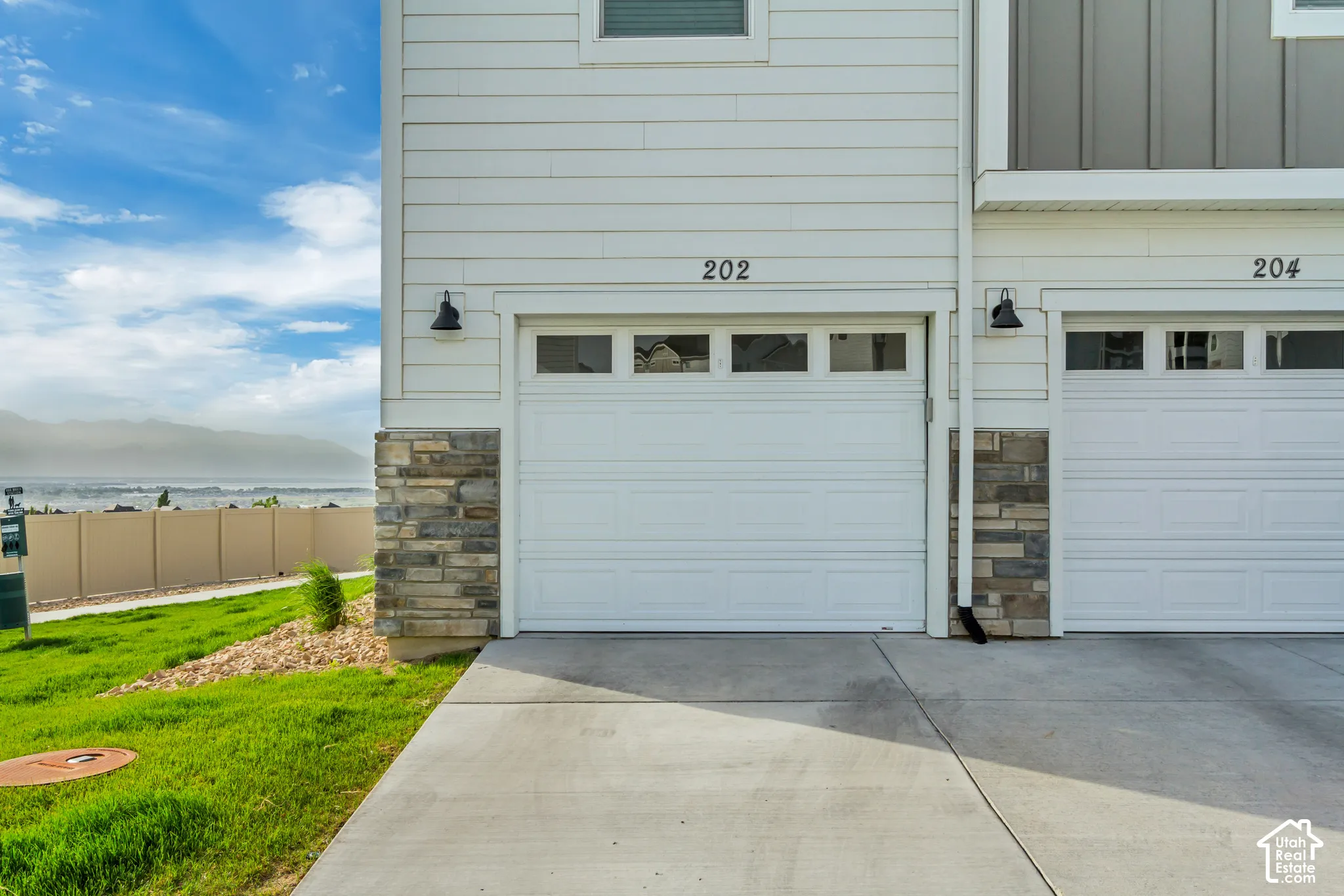 White horizontal siding exterior with stone accent columns, white paneled garage doors with upper window inserts, and black exterior lighting fixtures