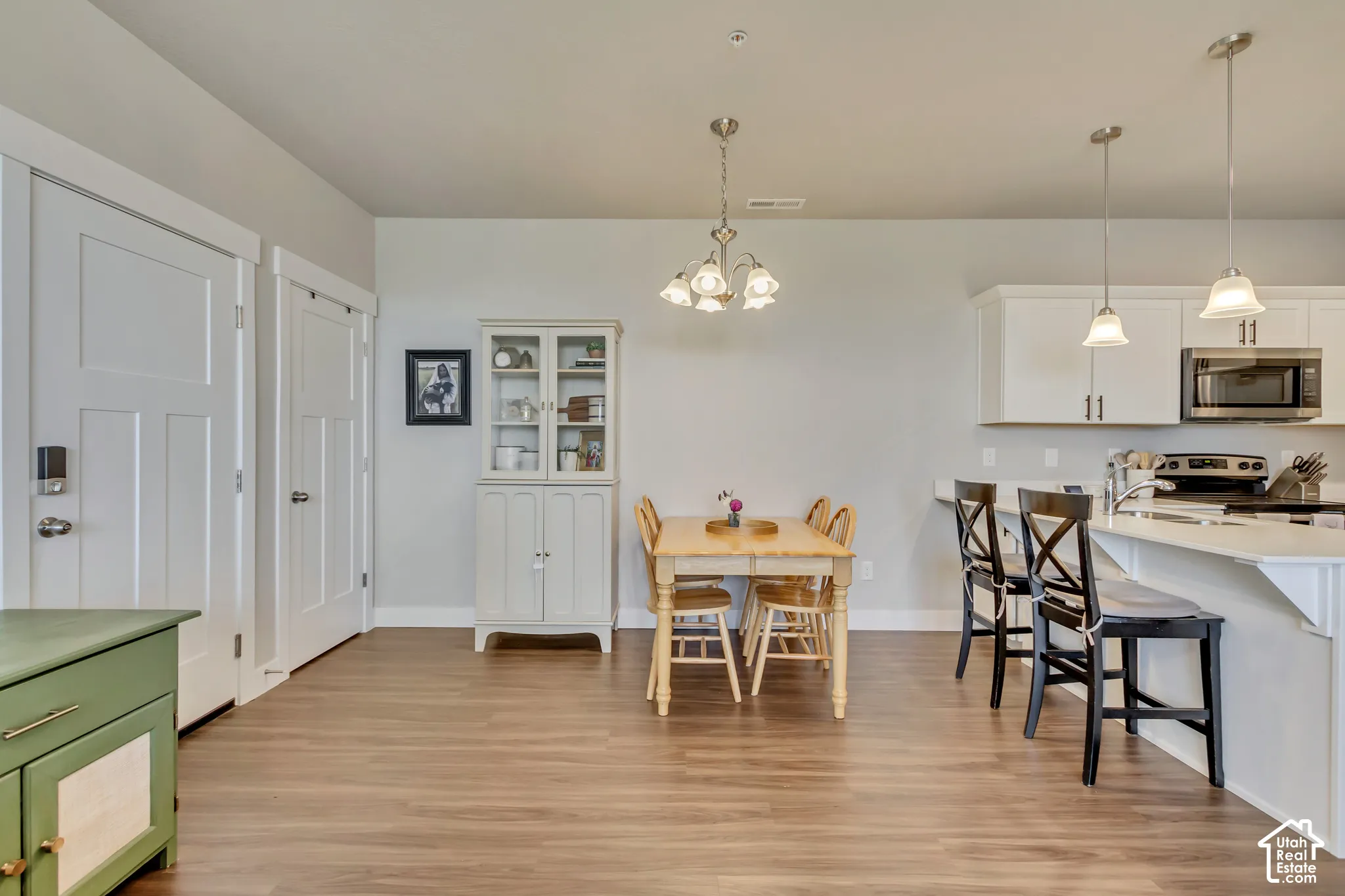 Wood-finish flooring throughout, white kitchen cabinetry, stainless steel microwave, and two pendant lights over the kitchen island