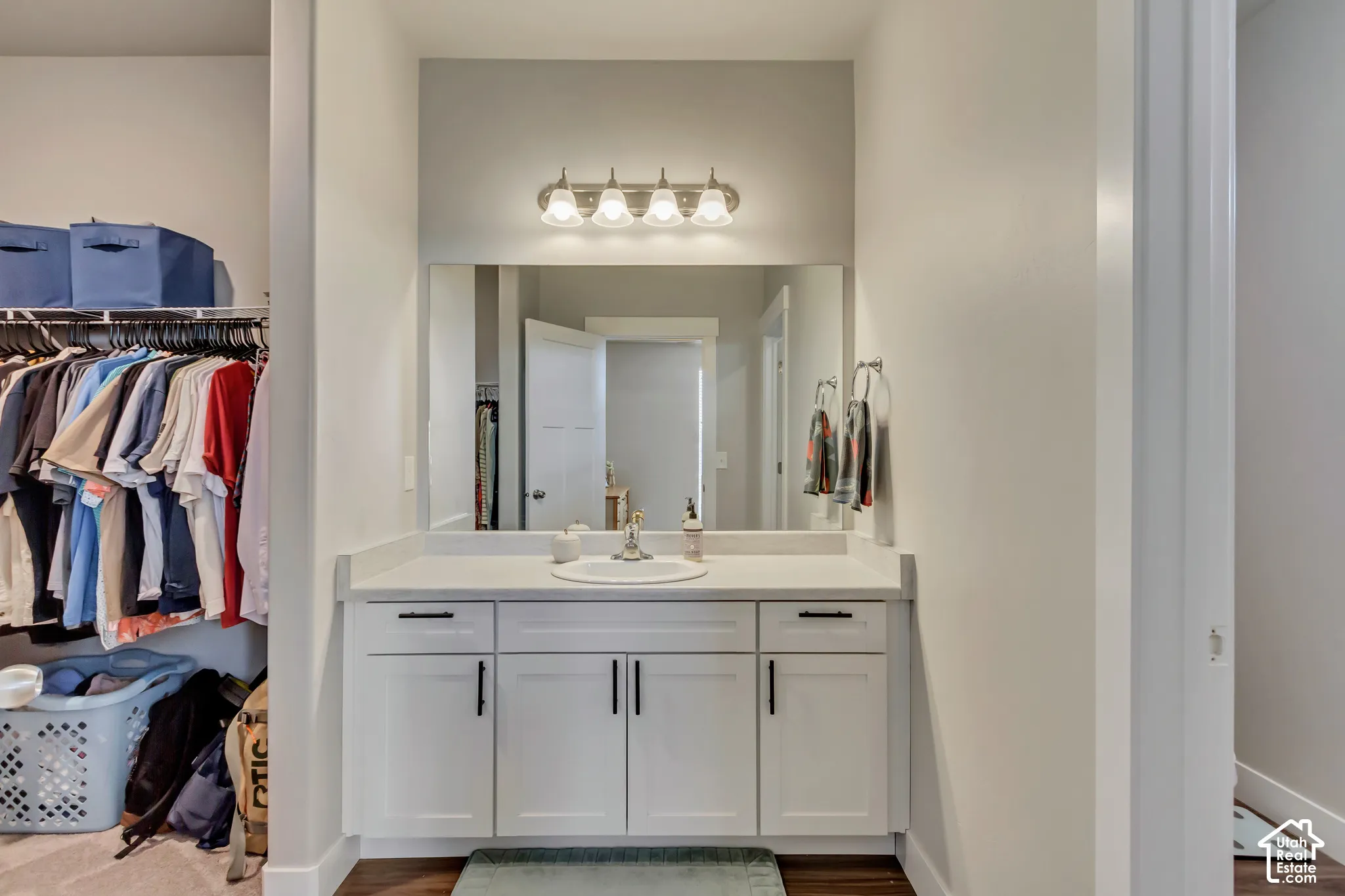 Vanity with a white countertop and integrated sink, white cabinetry with dark hardware, and a wall-mounted light fixture