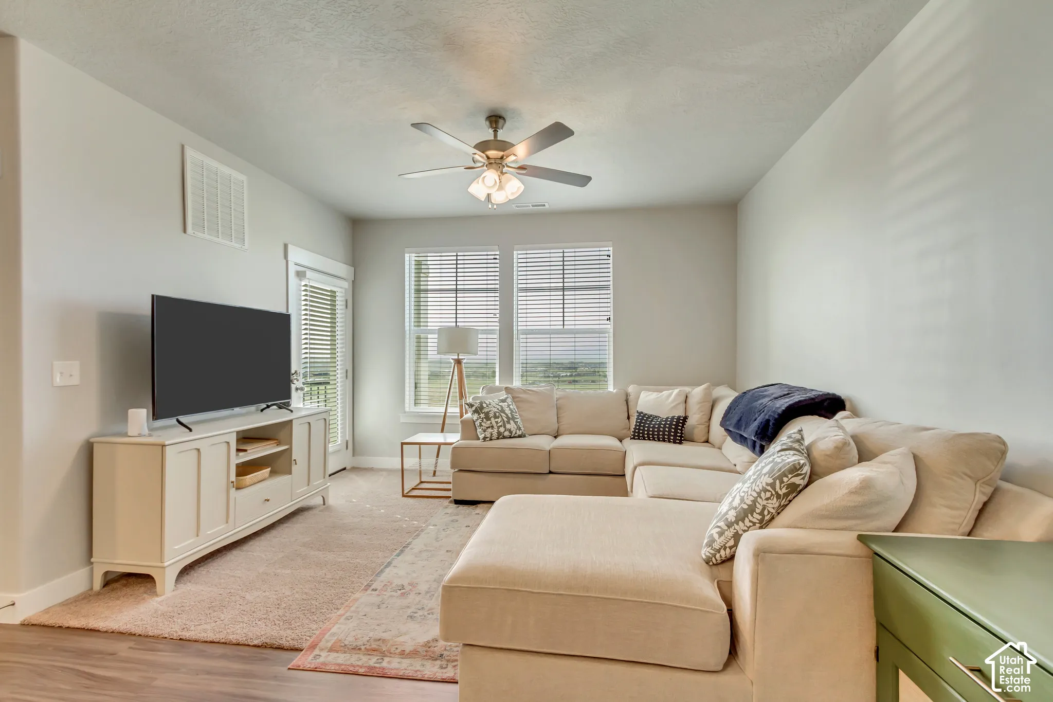 Spacious living area featuring wood-finish flooring, a ceiling fan, and large windows with blinds