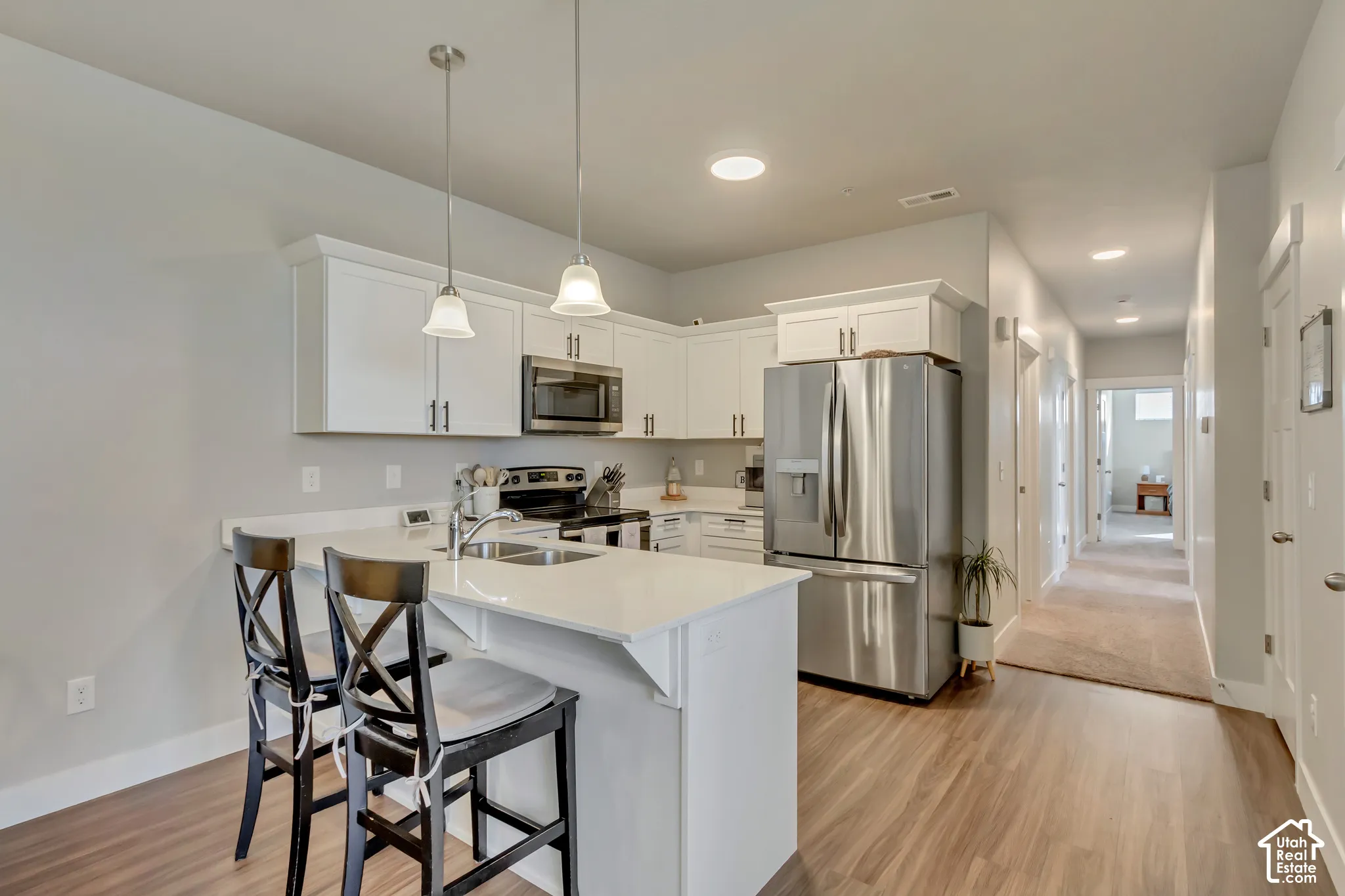 Modern kitchen featuring white cabinetry, stainless steel appliances, wood-finish flooring, recessed lighting, and pendant lighting fixtures