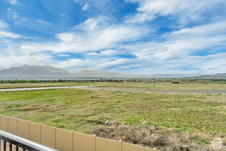 Expansive landscape featuring open fields, distant mountain ranges, and a clear sky with scattered clouds