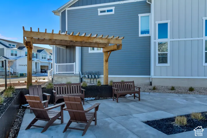 Patio area featuring a wooden pergola, concrete pavers, and landscaping with decorative rock and dark mulch