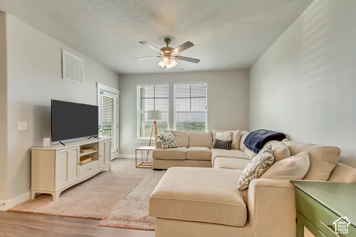 Spacious living area featuring wood-finish flooring, a ceiling fan, and large windows with blinds