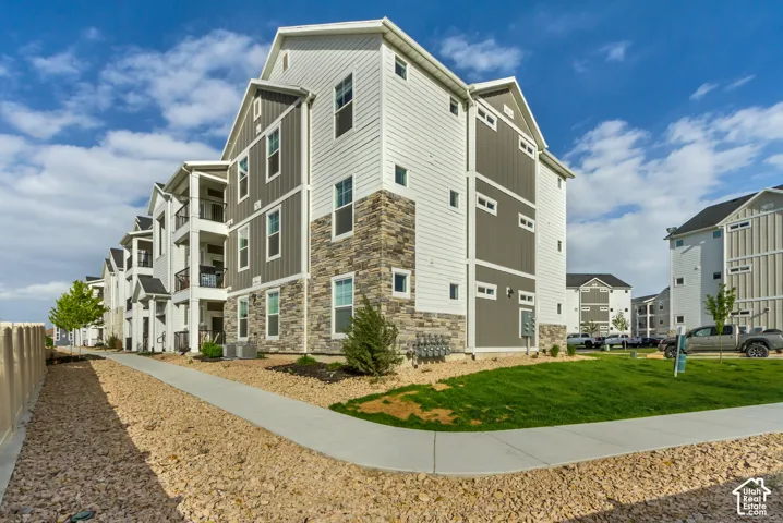 Multi-story building featuring a blend of horizontal siding and vertical paneling, stone veneer accents, individual balconies with dark railings, and a concrete pathway