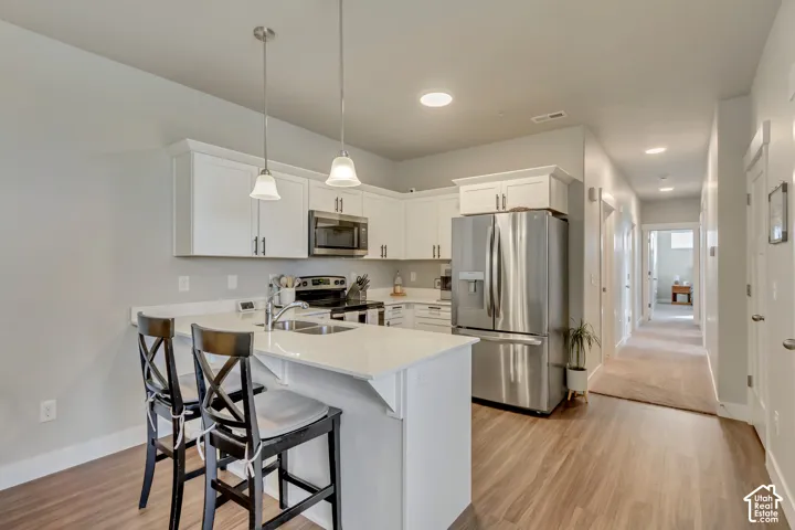 Modern kitchen featuring white cabinetry, stainless steel appliances, wood-finish flooring, recessed lighting, and pendant lighting fixtures