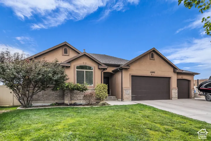Stucco exterior with brick detailing, arched entry window, attached two-car garage, single-car garage, and a manicured lawn
