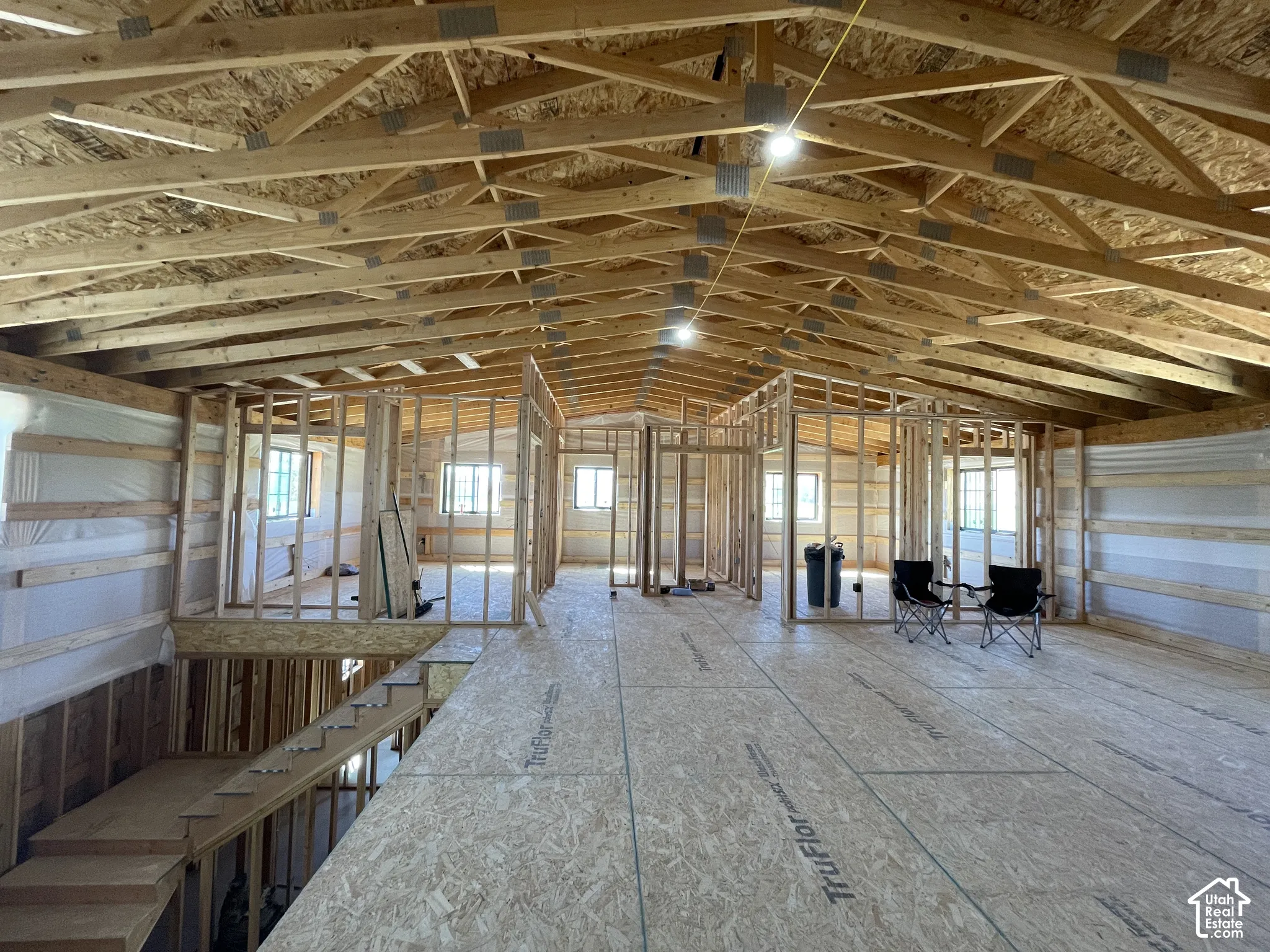 Framed interior space with exposed ceiling trusses, subfloor, and multiple window openings