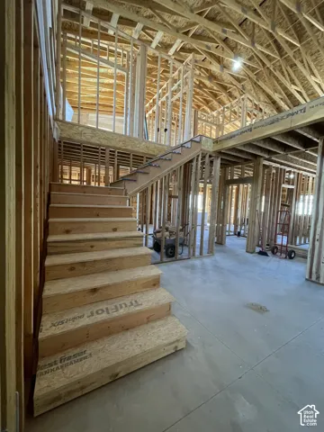 Vaulted ceiling with exposed wood framing, staircase with wood steps, and concrete flooring
