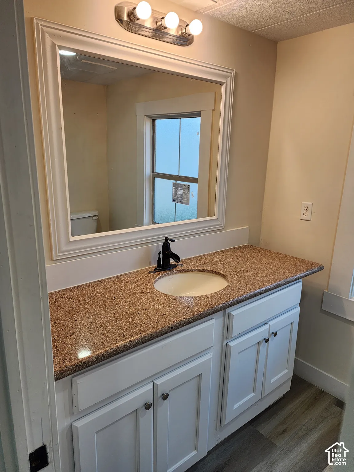 White vanity with shaker-style cabinetry, a speckled countertop, and an undermount sink