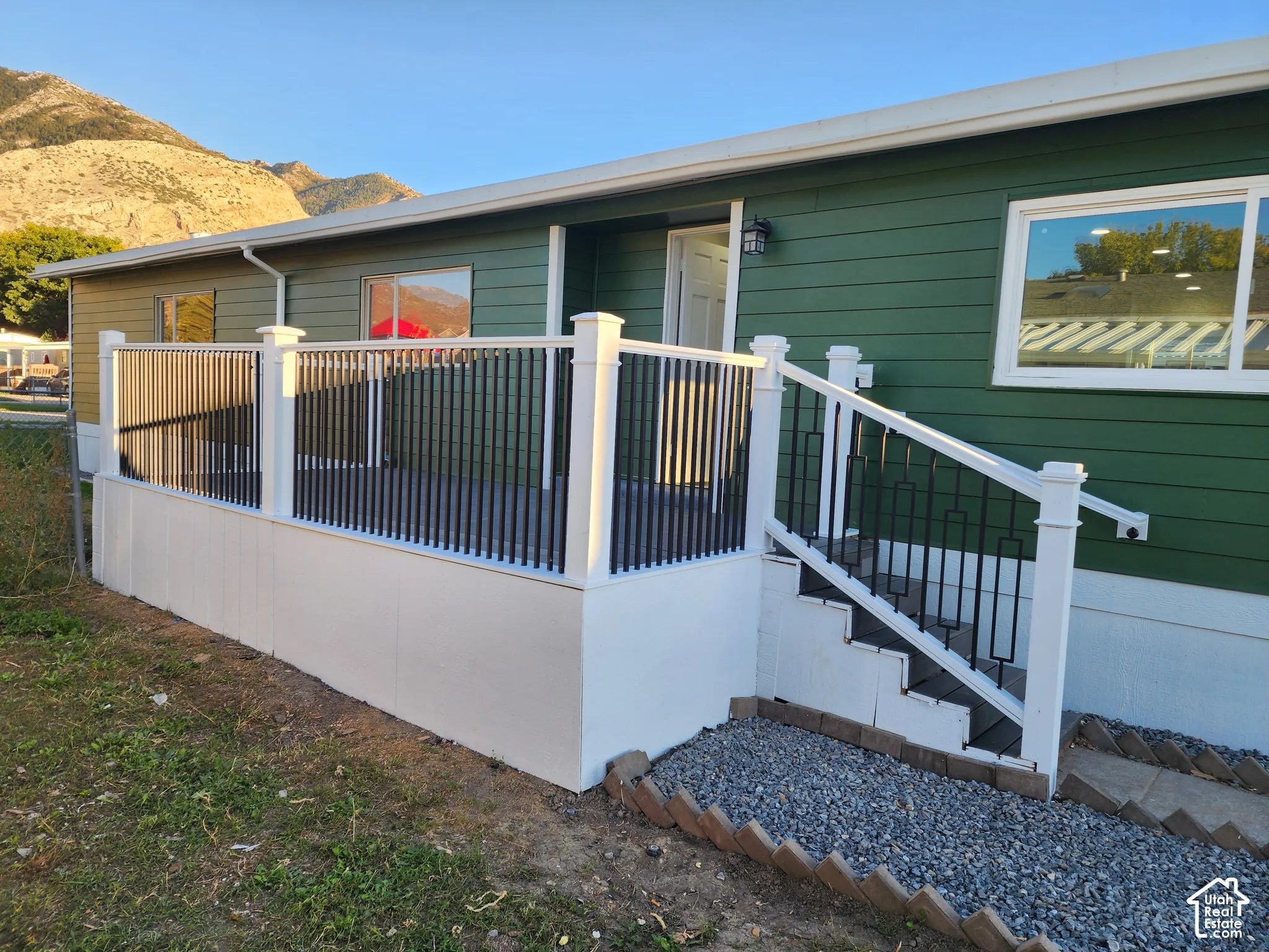 Exterior featuring horizontal siding, white-framed windows, an outdoor deck with white railings and black balusters, and a mountain backdrop