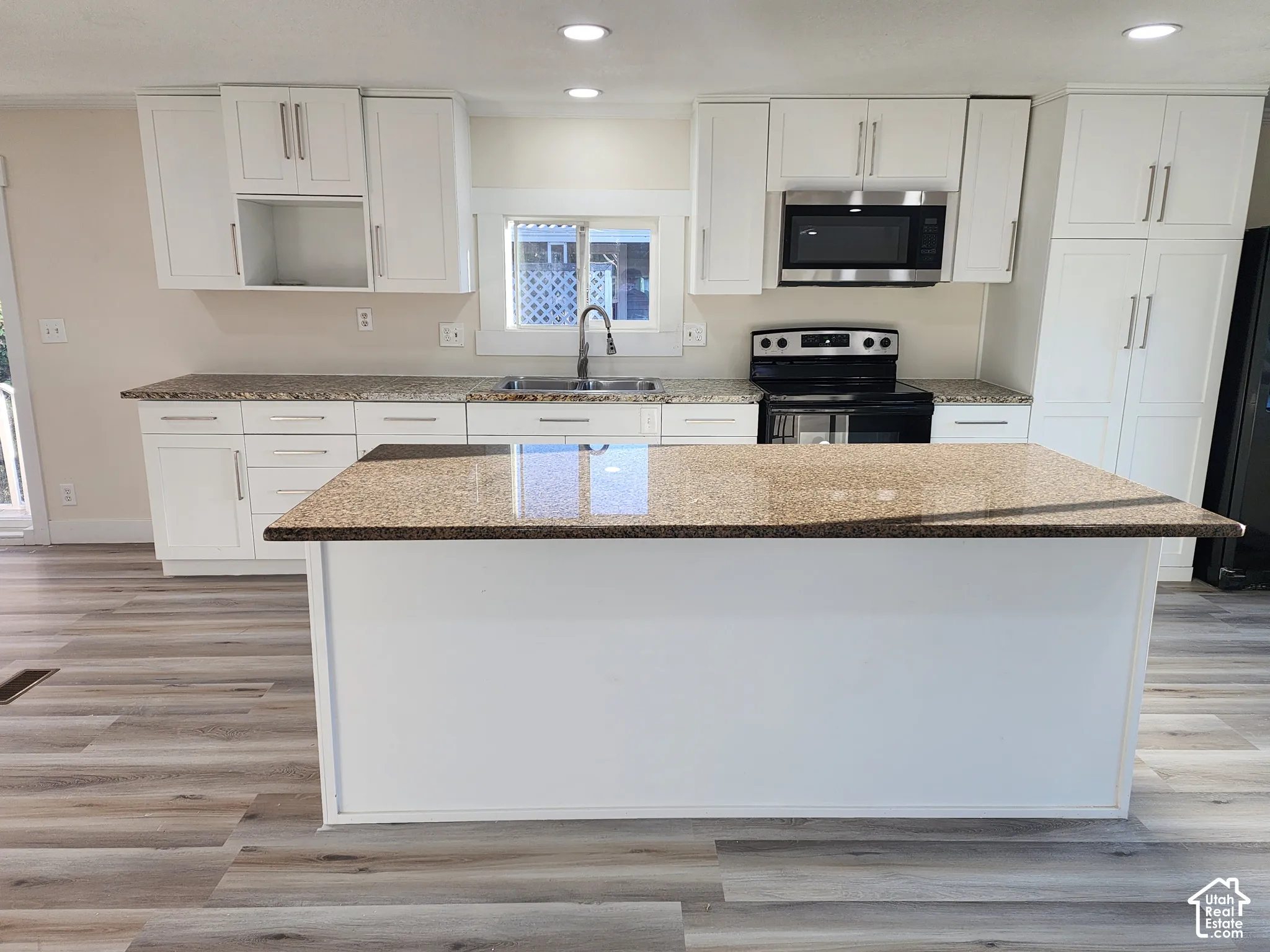 White cabinetry, granite-style countertops, stainless steel appliances, central island, and wood-finish flooring