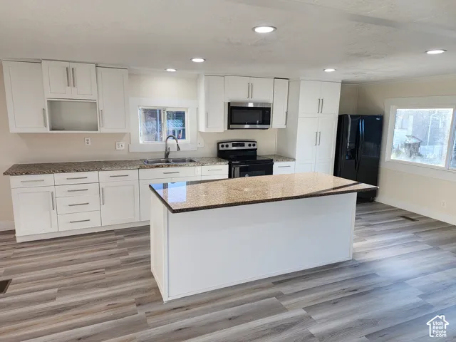 White cabinetry with brushed nickel hardware, granite countertops, stainless steel appliances, and wood-finish flooring