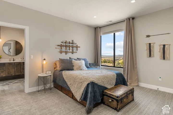 Recessed lighting, large window with expansive outdoor scenery, light-toned walls, textured carpeting, and an adjacent bathroom with a round mirror and wood-finish vanity